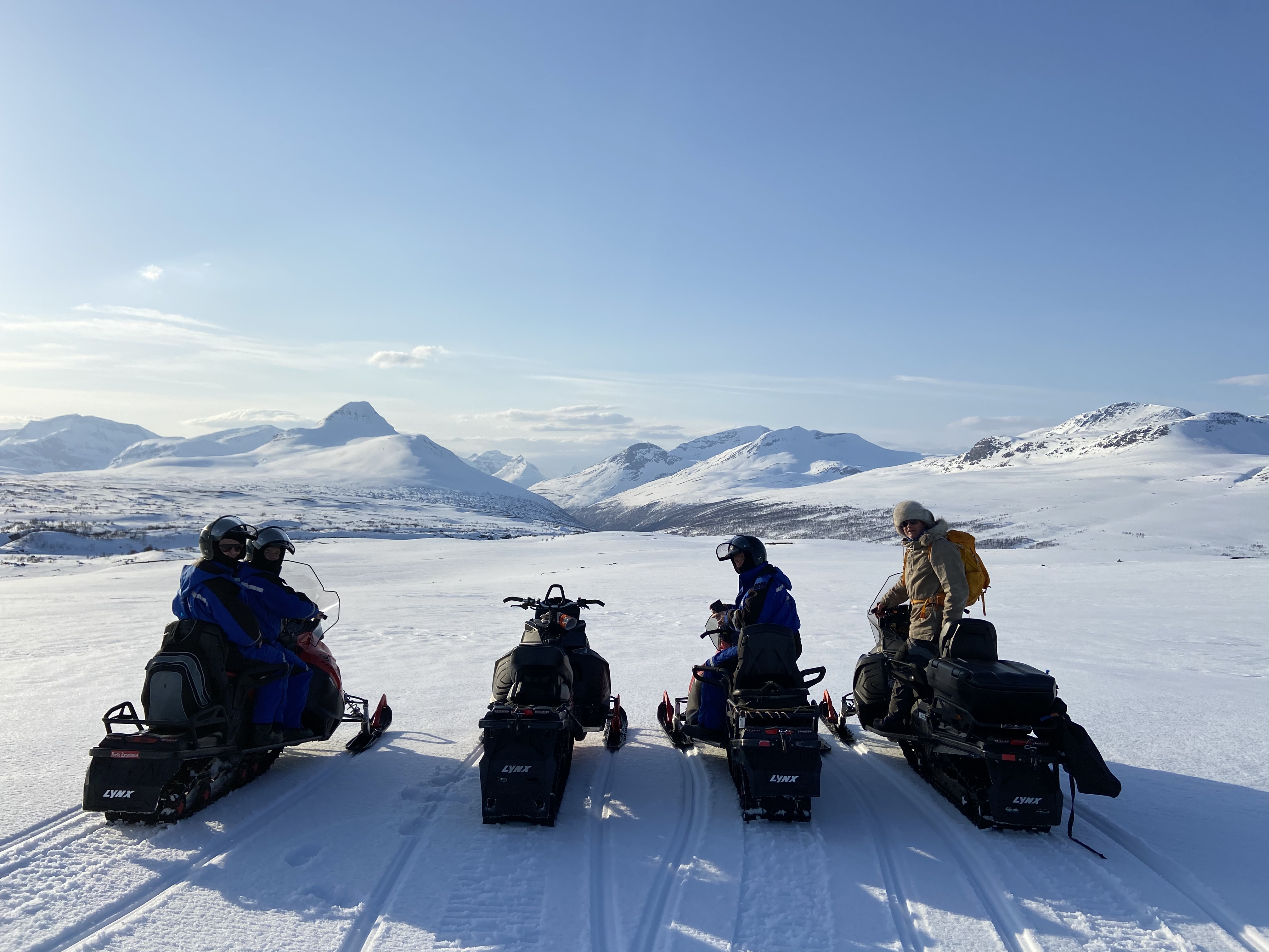 4 snowmobiles up in the mountains on a sunny spring day