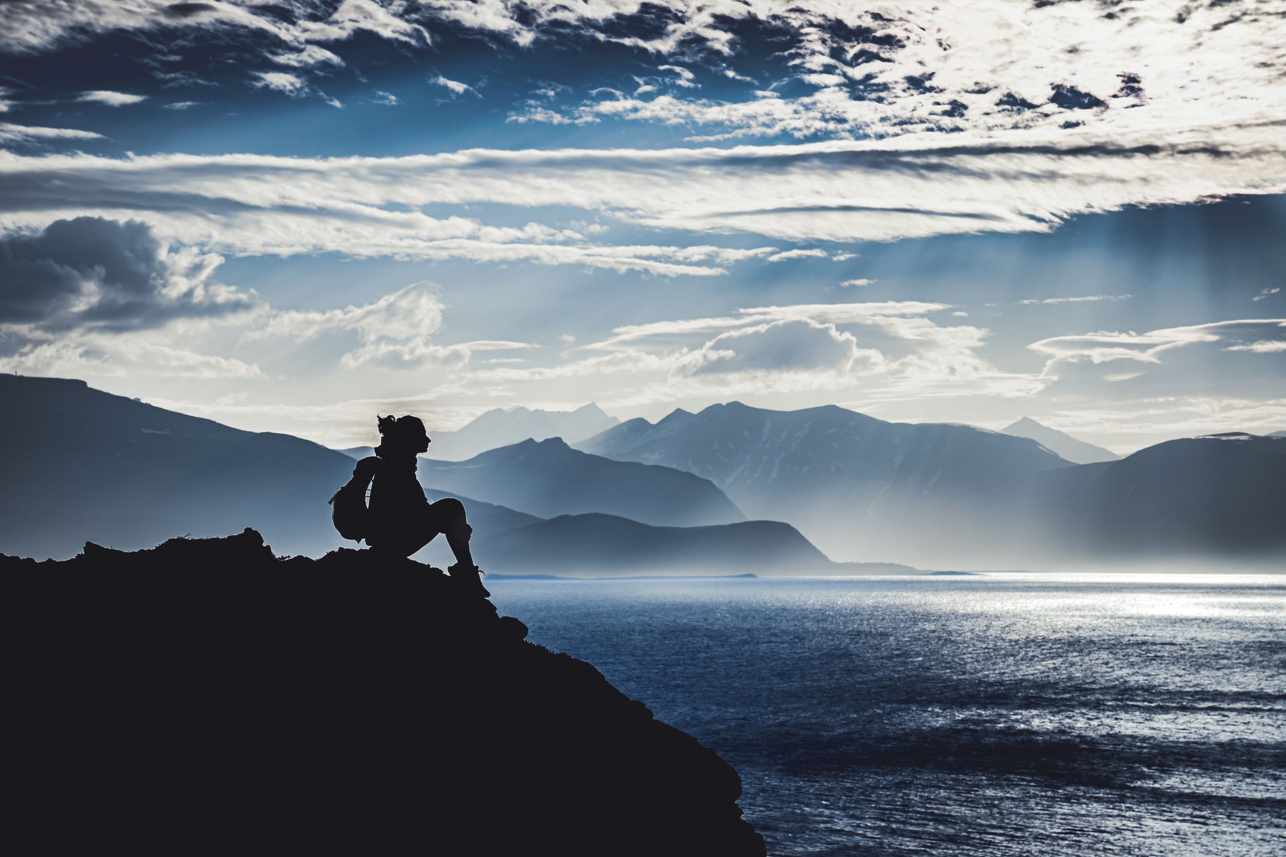 Silhuet of a person sitting by the sea and mountains on the background