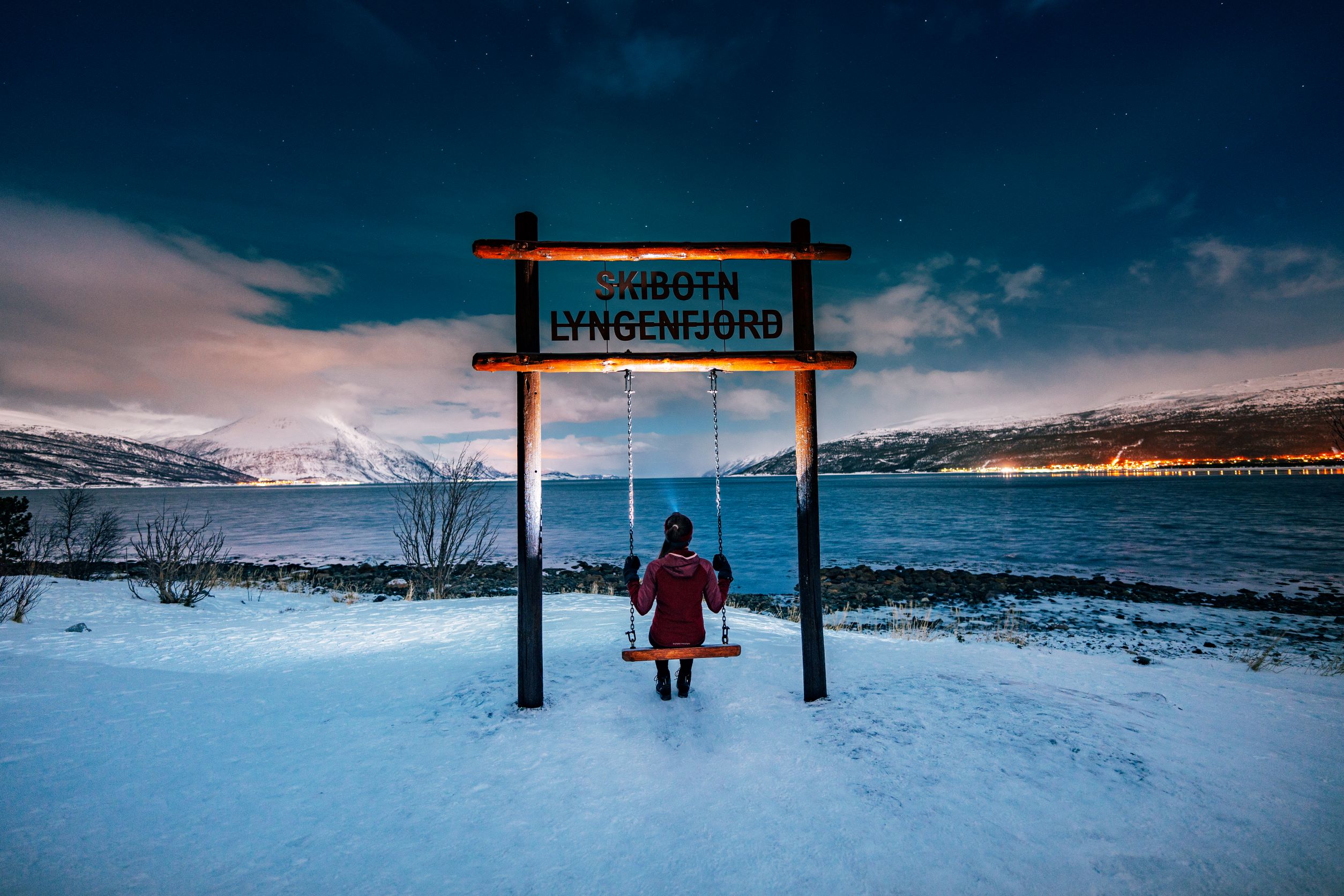 Person sitting in a swing and looking towards to see. Northern lights are in the sky. 