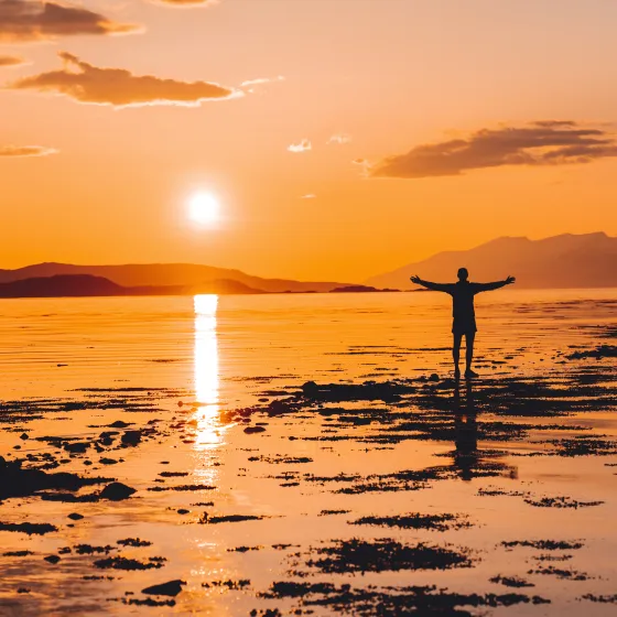 Man standing on a rock in the sea. Behind him you can see the midnight sun