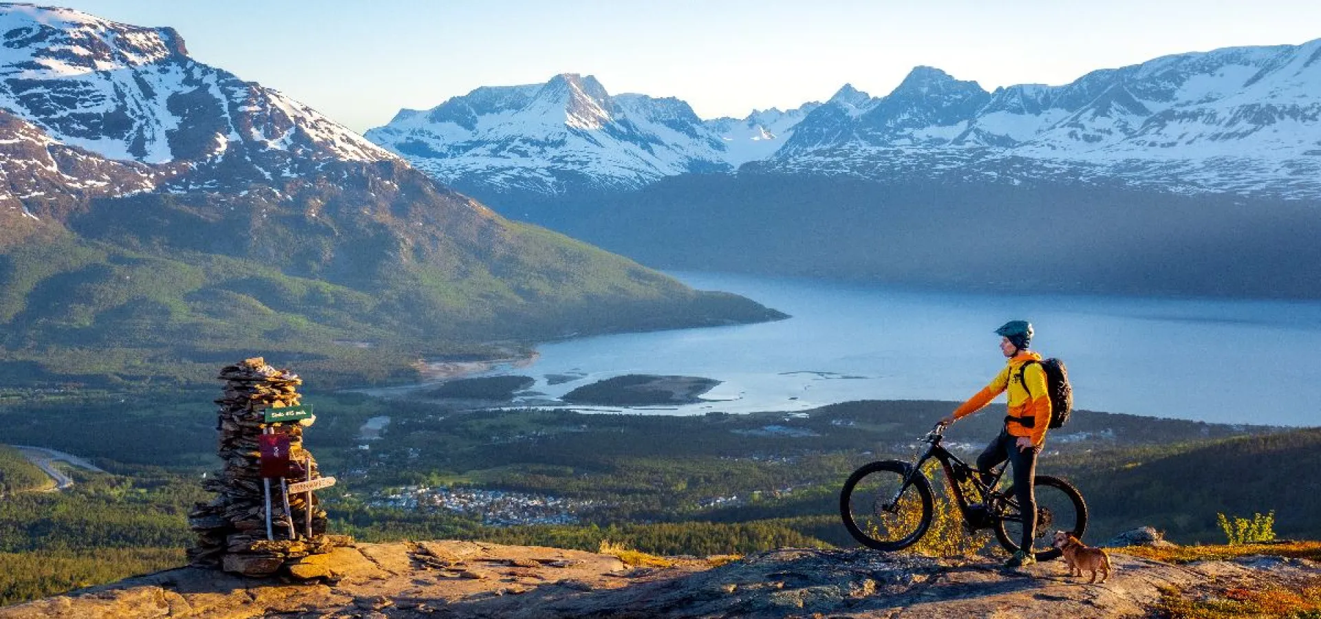 En person på sykkel høyt oppe på fjellet i midnattsol, utsikt til Skibotn
