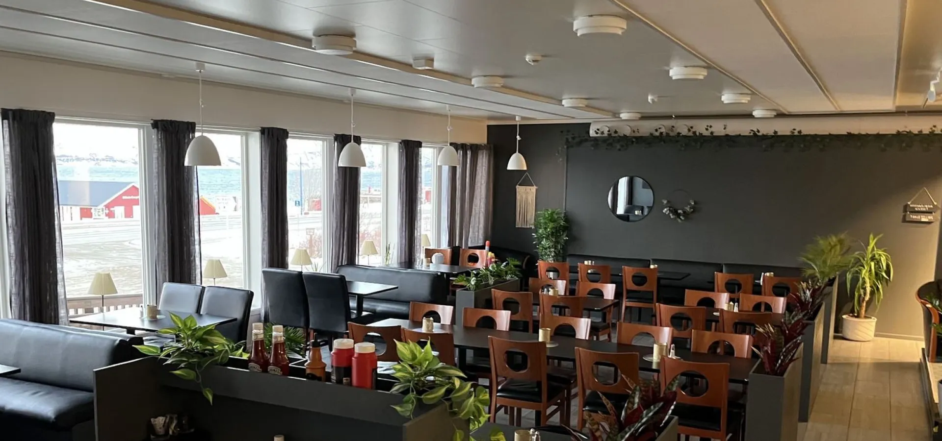 Interiøret i Arken Bistro, bord og stoler i en mørk stil, noen grønne planter innimellom