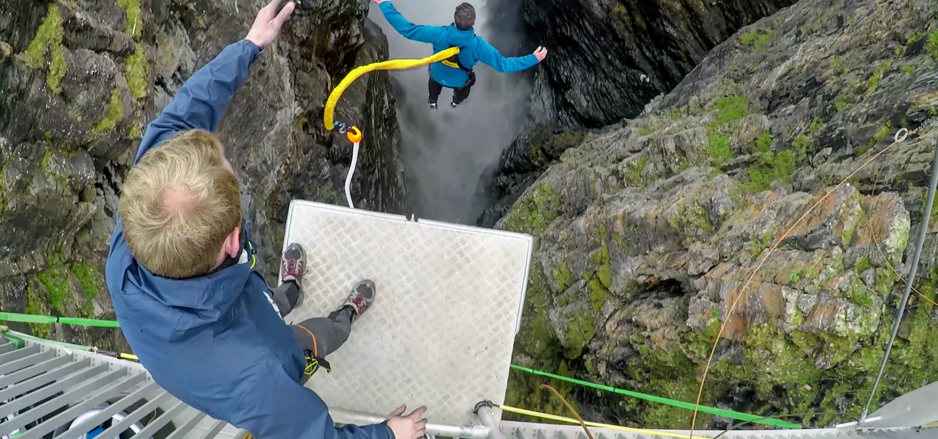 Person watching another person doing a bungee jump near a waterfall