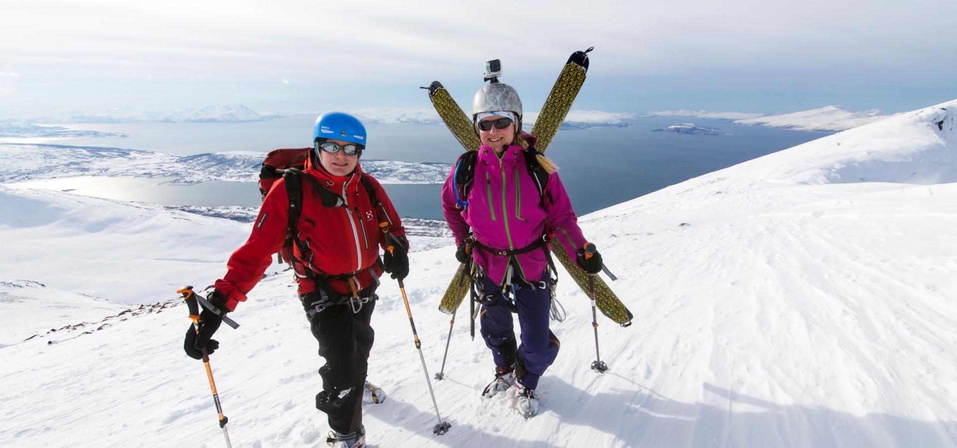 To skientusiaster på toppen av Russelvtinden, med fjorden i bakgrunnen