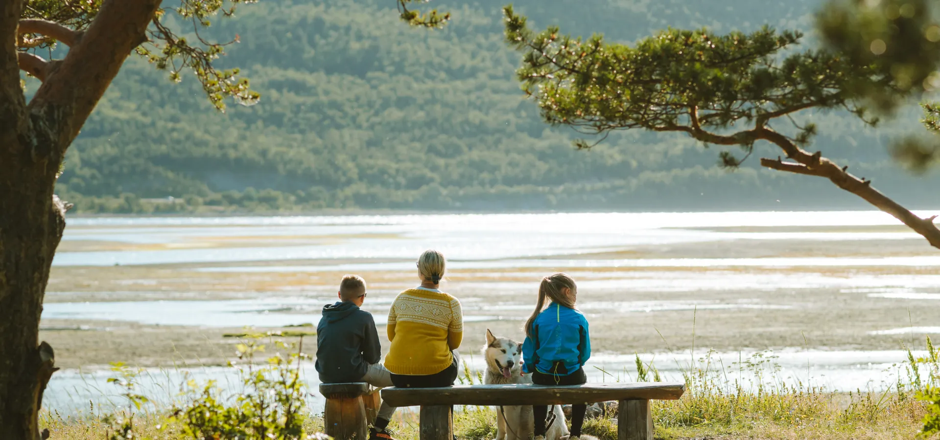 Familie med hund sitter på en benk og ser utover Skibotndeltaet