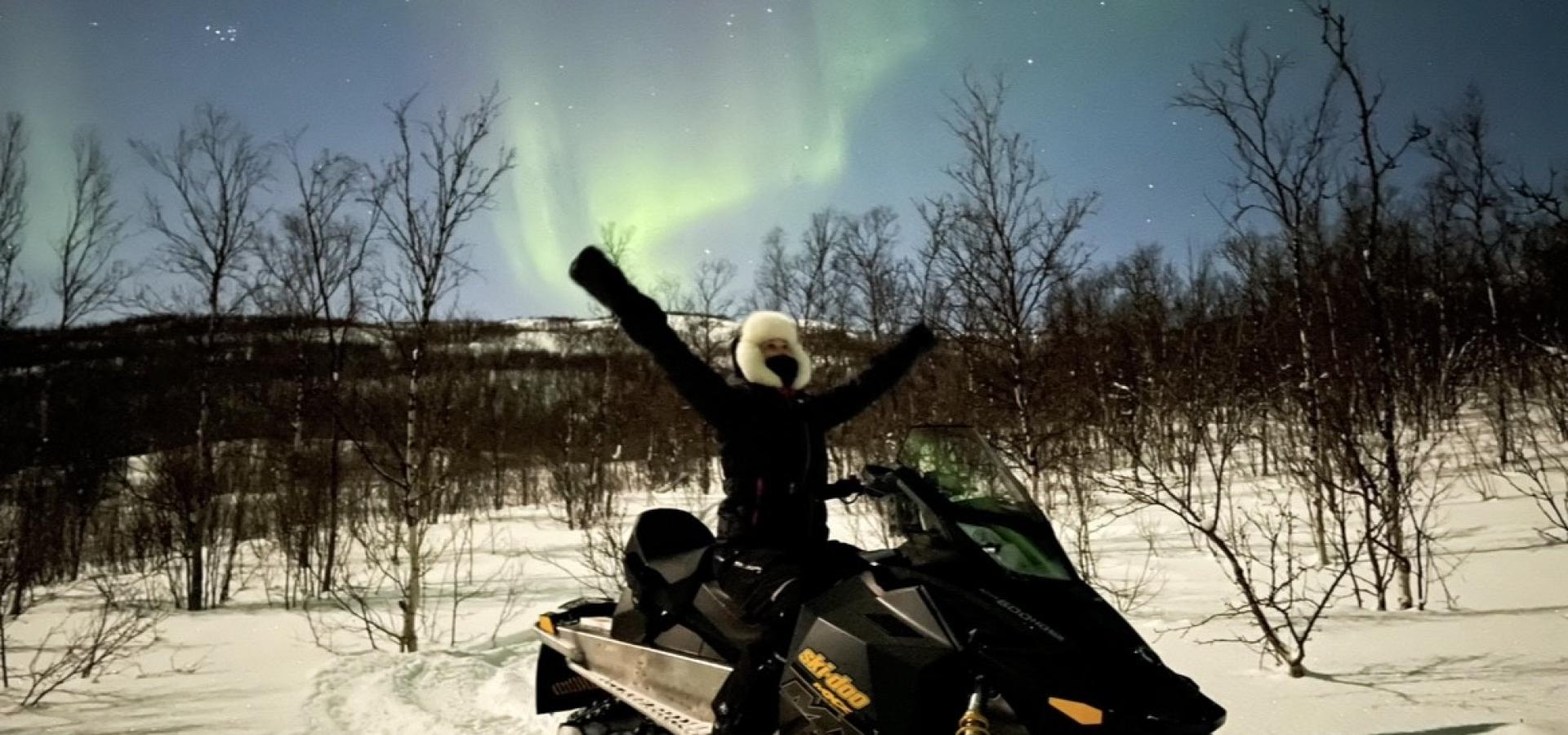 woman on snowmobile under northern lights