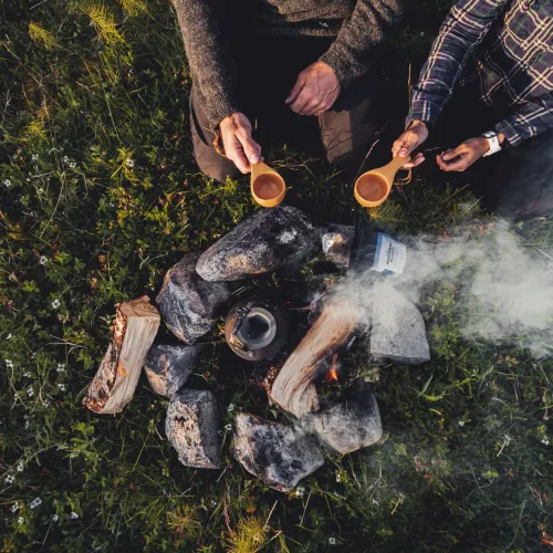 Two hands holding coffee mugs by a campfire