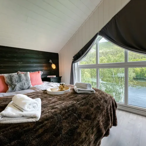 Mollis suite på reisastua lodge. Seng med brunt pledd, hvitt pledd og håndduker.