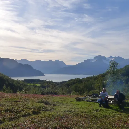 Two persons sitting on a outdoor table, in the background the fjord and the mountains