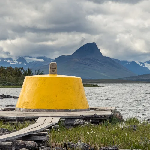 The yellow painted border marker at the three country cairn with the lake and norwegian mountains in the background