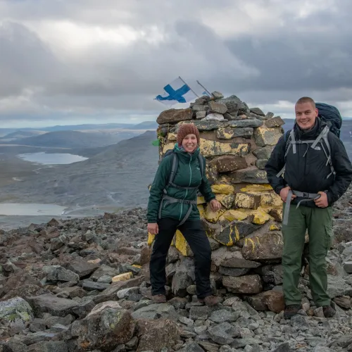 Two hikers by the cairn at Halti, with a view towards some lakes