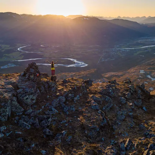 Person enjoying the view of Storslett from the peak Jyppyrä in the evening sun