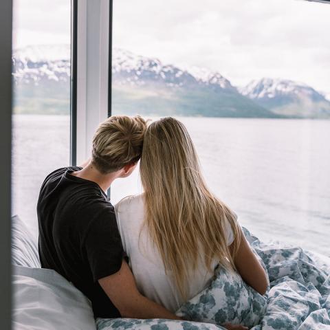 To som sitter på senga og ser ut på Lyngenfjorden rett utenfor