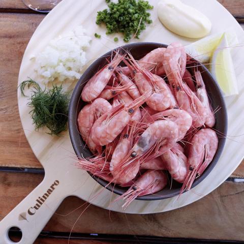 Shrimps in a bowl on a wooden surface with lemon and green around it, photo taken from above