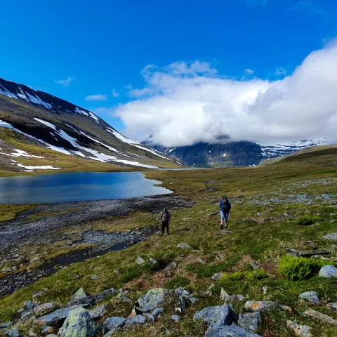Two hikers in the mountains with a small lake in the background