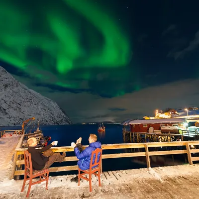 two persons sitting outside on the pier enjoying the northern lights