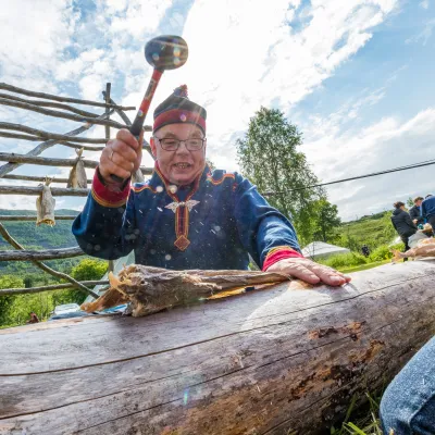 En mann i kofte som sitter å banker tørrfisk ute i solskinn