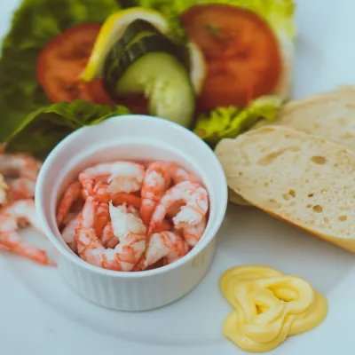 Reker i en liten skål, salat og loff på et fat