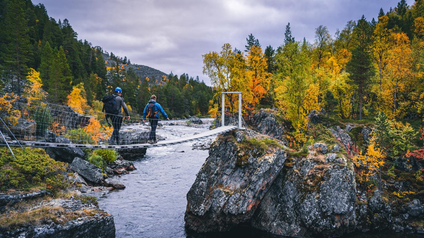 Two men hiking, and crossing a bridge in Reisa National park