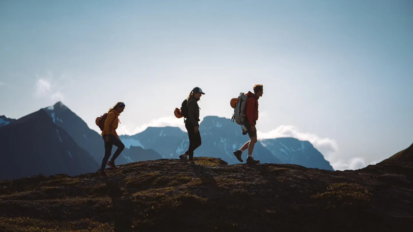 3 personer vandrer på fjellet, sees som siluetter