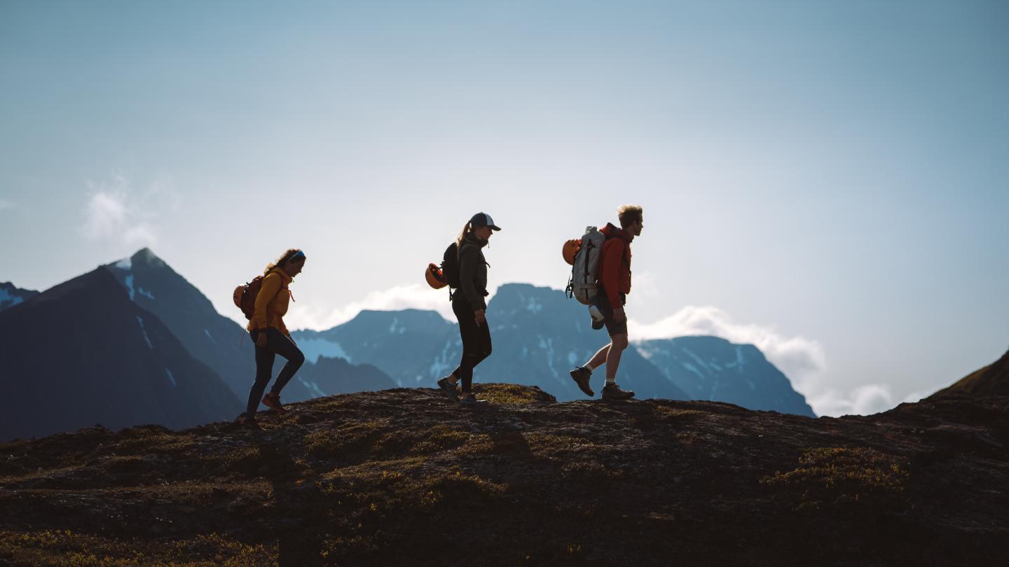3 personer vandrer på fjellet, sees som siluetter