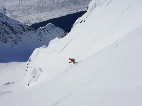 Mann kjører ned en fjellside på ski. I bakgrunnen kan du se havet og fjell.