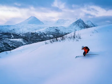 En person står på ski ned en fjellside