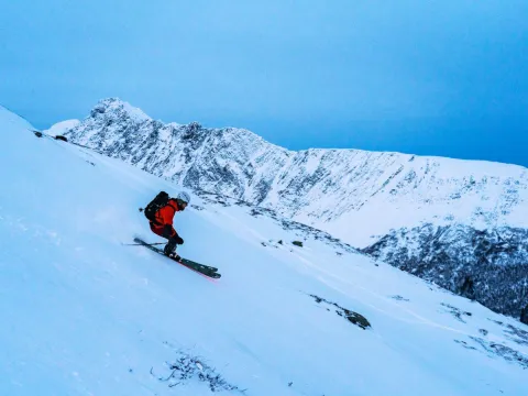 Mann kjører ned en fjellside på ski. I bakgrunnen kan du se fjell.