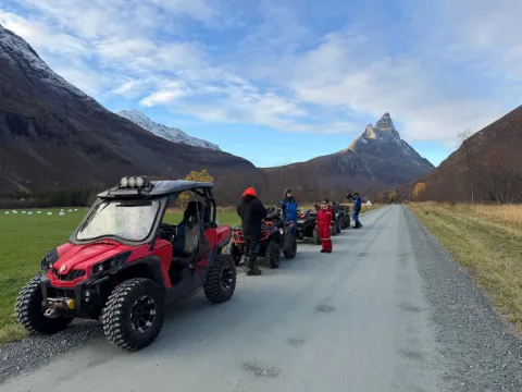 Mange firhjulingen på rekke og rad etter en grusvei. I bakgrunnen kan du se et jorde og høye fjell.
