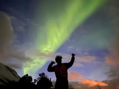 En mann flekser med musklene under nordlyset.