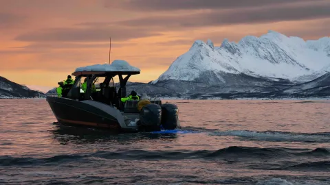 En båt på fjorden, snødektefjell i bakgrunnen. Solnedgangsfarger