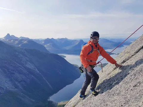 En mann klatrer opp en fjellside iført klatreutstyr.