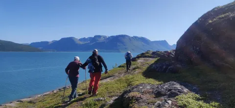 Tre mennesker går på tur en sommerdag. Du kan se havet og fjell.