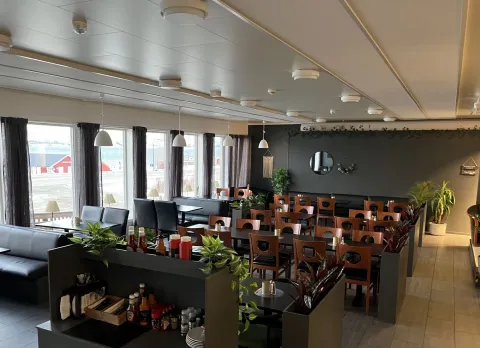 Interiøret i Arken Bistro, bord og stoler i en mørk stil, noen grønne planter innimellom