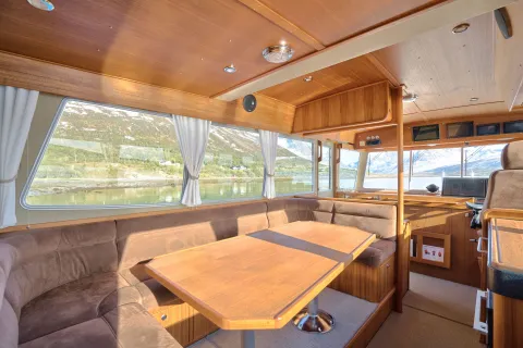 Sitteområde ombord på targaen. Brunfarget sofa og bord i tre.