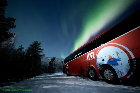 The classic red Arctic Route bus under the northern lights