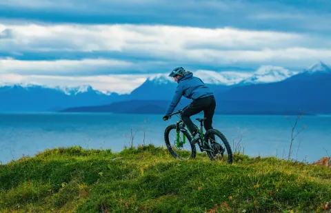 Person som sykler på sti, fjord og fjell i bakgrunnen